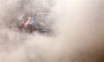 A Bangladeshi rickshaw puller rides past smoke created by burning waste materials on a street in Dhaka. Photograph Anado